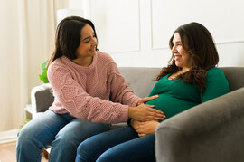 A happy pregnant woman sits on the couch being checked by her doula