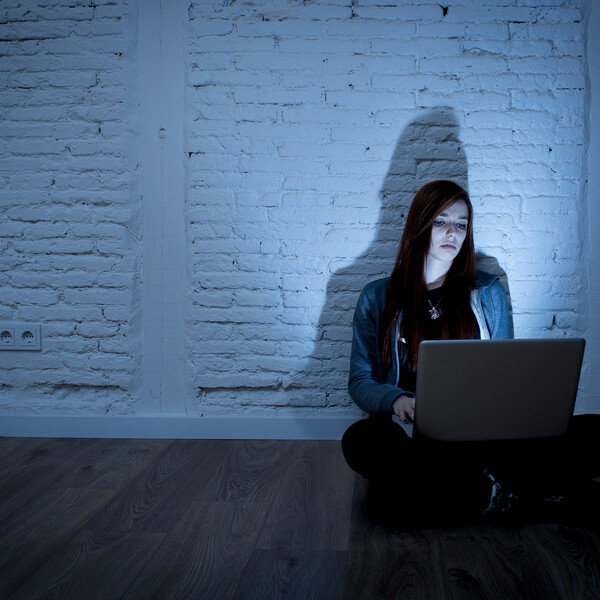 A woman sits on a floor looking at an open laptop that's in her lap