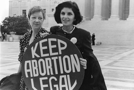 A black and white photo of Norma McCorvey and Gloria Allred standing outside the Supreme Court holding a sign that reads "Keep Abortion Legal"
