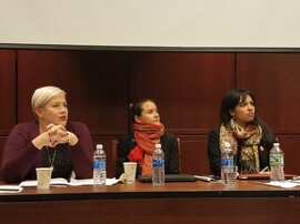 Three women sit at a table with notes and computers in front of them.