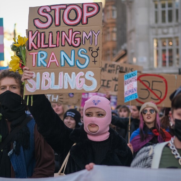 A woman at a protest holding a sign that reads "Stop Killing My Trans Siblings"