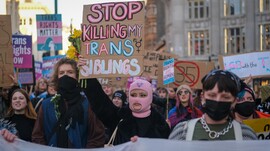 A woman at a protest holding a sign that reads "Stop Killing My Trans Siblings"