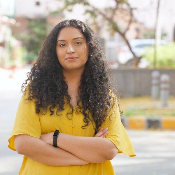 A South Asian woman stands with her arms crossed and looks at the camera