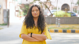 A South Asian woman stands with her arms crossed and looks at the camera