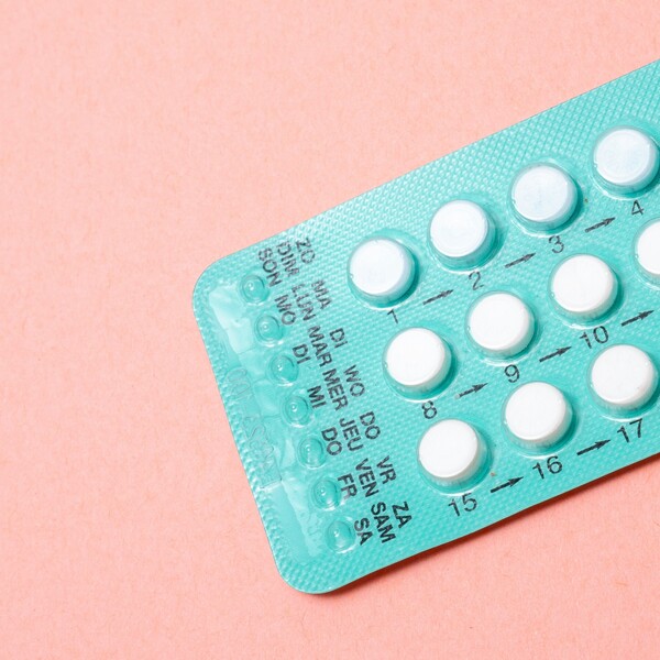 A pink background with a blue pack of white birth control pills