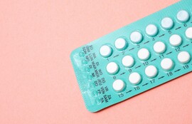 A pink background with a blue pack of white birth control pills