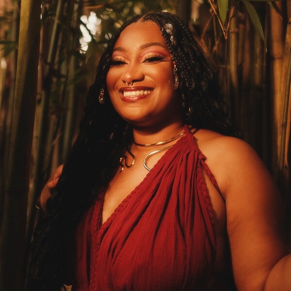 A black woman in a red dress with braids smiling