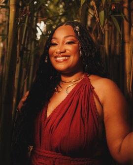 A black woman in a red dress with braids smiling