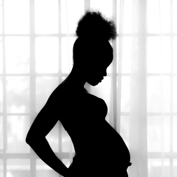 A silhouette of a Black woman standing in front of a bright window