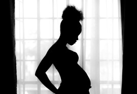 A silhouette of a Black woman standing in front of a bright window
