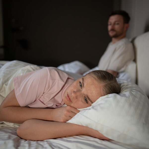A woman lies in bed with a sad or disappointed look on her face
