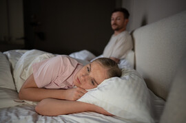 A woman lies in bed with a sad or disappointed look on her face