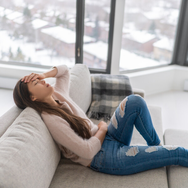 A woman lays on a couch with her hand on her head and her eyes closed