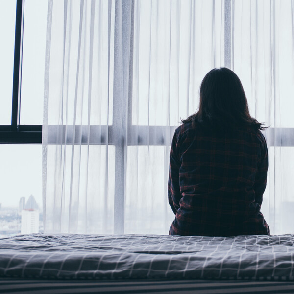 The back of a woman sitting on a bed in front of a window