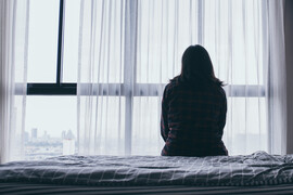 The back of a woman sitting on a bed in front of a window