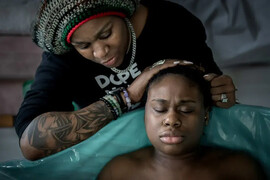 A Black woman giving birth at home in a pool with a midwife