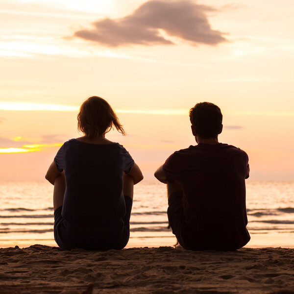 A young couple sits together on the beach