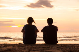 A young couple sits together on the beach