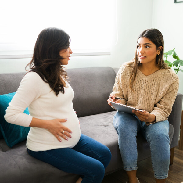 A pregnant woman talks to another woman who is holding a clipboard