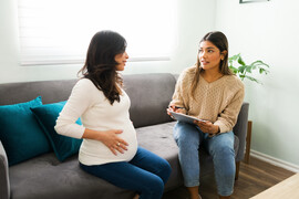 A pregnant woman talks to another woman who is holding a clipboard