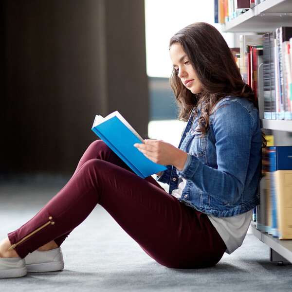A girl reads a book on the floor of a library