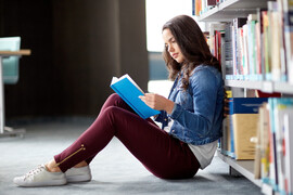 A girl reads a book on the floor of a library