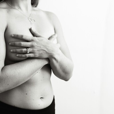 A black and white photo of a woman's torso with her hands covering her breasts