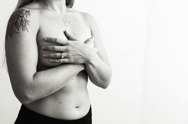 A black and white photo of a woman's torso with her hands covering her breasts