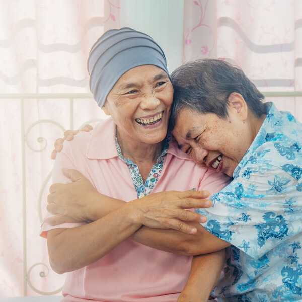 Older Asian woman with cancer hugs friend
