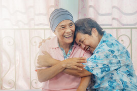 Older Asian woman with cancer hugs friend