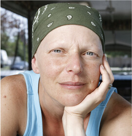 A woman with a green bandana on her head looks at the camera