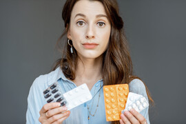 A woman with a straight face holding birth control pills