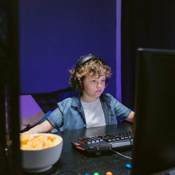 A white boy with curly hair sits on a computer in a dark room