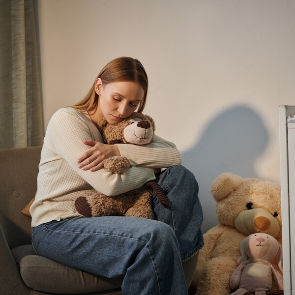A woman sits in an empty nursery hugging a teddy bear