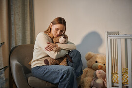 A woman sits in an empty nursery hugging a teddy bear