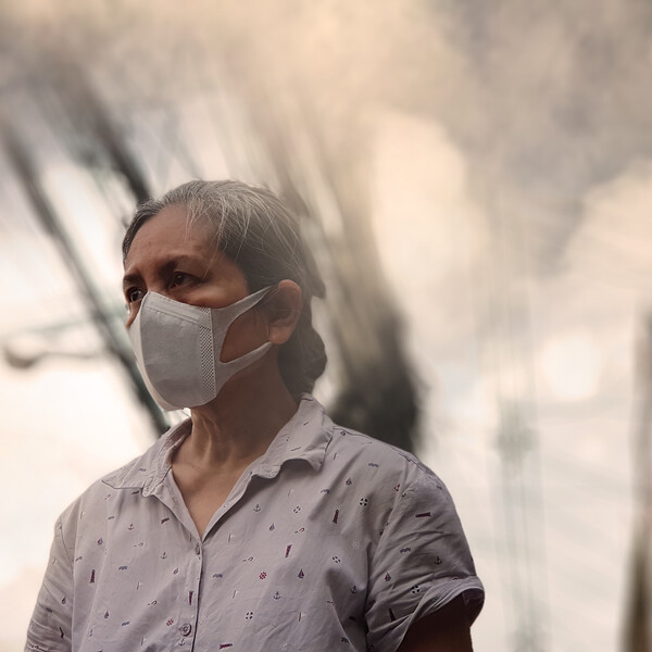 An older woman stands in a circle of smoke in a city
