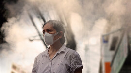 An older woman stands in a circle of smoke in a city