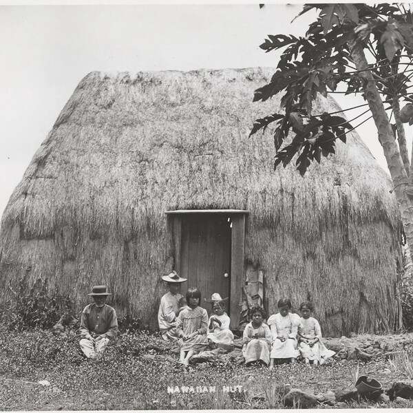 A grass hut with a Hawaiian family out front