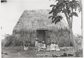 A grass hut with a Hawaiian family out front