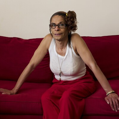 A lighter-skinned Black woman sits on a red couch in red pants and a white tank top