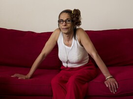 A lighter-skinned Black woman sits on a red couch in red pants and a white tank top