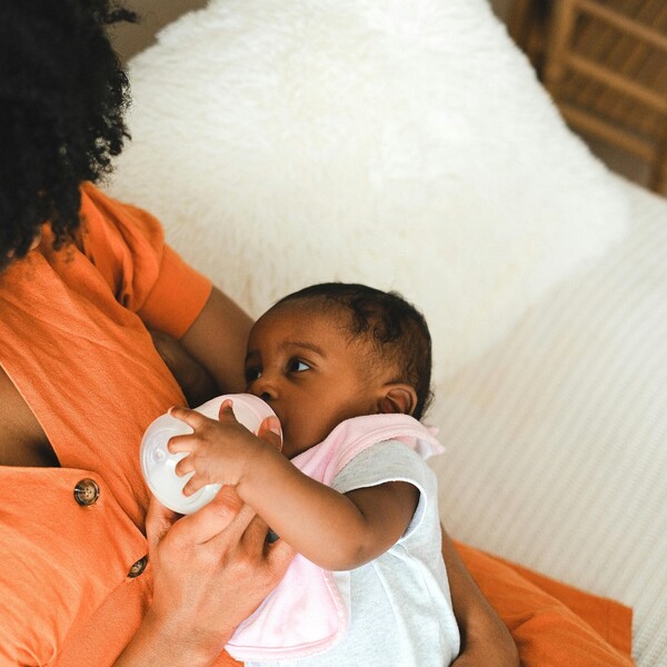 A Black woman with curly hair feeds a baby with a bottle