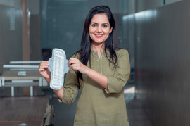An Indian woman smiles and holds up a menstrual pad