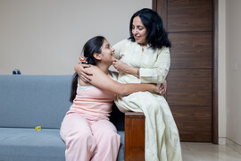 An Indian mother and daughter set on a couch together, smiling