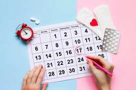 A calendar with a date circled, pads, pills, and a clock