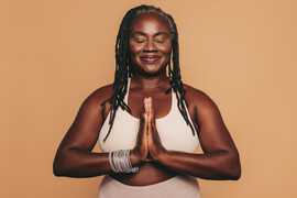 Mature woman meditating with her eyes closed and her hands in prayer position. Black woman with dreadlocks practicing yoga in a studio. Happy middle-aged woman maintaining a healthy lifestyle.