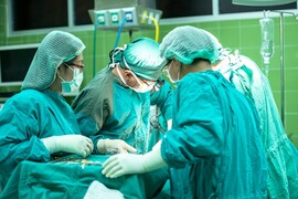 An image of a surgery taking place; surgeons stand around a bed looking on