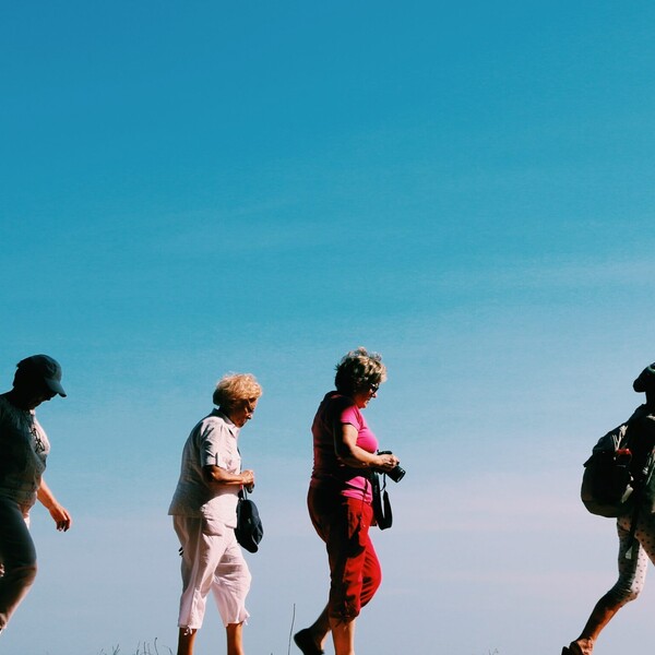 Four older women walk outside. They are in a mix of sun and shadow.