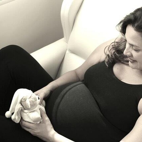 A black and white photo, a pregnant woman wearing a black top and black leggings is holding a small teddy bear.