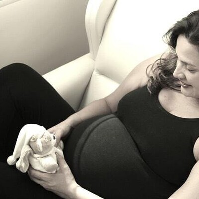 A black and white photo, a pregnant woman wearing a black top and black leggings is holding a small teddy bear.